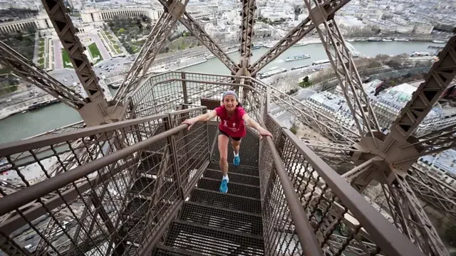 Jovem subindo as escadarias da Torre Eiffel, com vista panorâmica de Paris, na França
